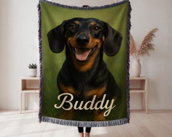 May include: A woven throw blanket featuring a portrait of a black and tan dachshund with its mouth open in a smile. The name Buddy is printed in a cream-coloured script font across the lower portion of the blanket, which has fringed edges.