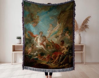 Puede incluir: Manta tejida con una pintura clásica que representa figuras en un cielo nublado. La obra de arte utiliza tonos azules, rojos y crema. La manta tiene un borde con flecos. La manta está sujeta por una persona.