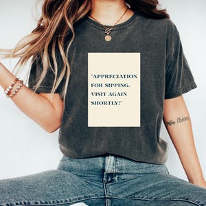 May include: A dark grey t-shirt with the text "APPRECIATION FOR SIPPING. VISIT AGAIN SHORTLY!" printed on the front.