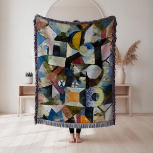 May include: A colorful woven throw blanket with a geometric abstract design. The blanket features a variety of shapes and colors, including blue, yellow, brown, and orange. The edges are finished with a fringe.