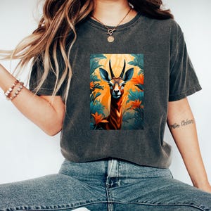 May include: A dark gray t-shirt with a graphic print of a brown and orange deer with large antlers standing in a jungle setting with green and orange leaves.