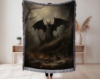 May include: A woven throw blanket with a dark fantasy illustration of a horned, winged demon in a desolate, fiery landscape. The blanket has a fringed edge with blue, purple, and black hues.