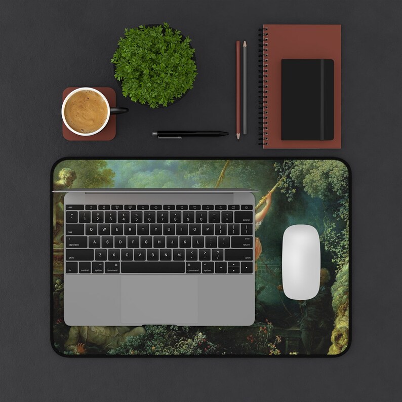 May include: A laptop computer with a keyboard and trackpad is on a desk mat with a colorful painting of a garden scene. A cup of coffee, a potted plant, a notebook, and two pencils are also on the desk.