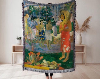May include: Woven throw blanket featuring a colorful reproduction of Paul Gauguin's "La Orana Maria" painting. The artwork depicts three women in a tropical setting, with vibrant greens, blues, and reds. The blanket has a fringed edge.