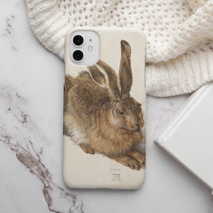 May include: A phone case with a brown and white illustration of a hare. The illustration is in a vintage style and includes the text "1503" and a symbol.