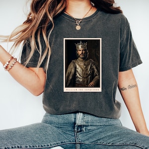 Może przedstawiać: Szary t-shirt z nadrukiem w stylu vintage przedstawiającym Wilhelma Zdobywcę w koronie i królewskich szatach. Pod obrazem znajduje się napis "William the Conqueror".