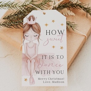 May include: A white gift tag with a pink ballerina illustration. The tag has gold stars and the text "HOW sweet IT IS TO Dance WITH YOU Merry Christmas! Love, Madison".