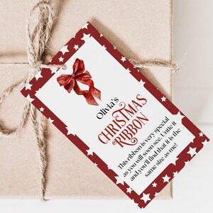 Puede incluir: Una caja de regalo marrón atada con hilo de bramante, con una etiqueta navideña roja y blanca. La etiqueta dice "Olivia's Christmas Ribbon" e incluye una ilustración de lazo y texto.