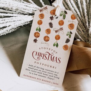 Könnte beinhalten: Ein braunes Papier-Geschenk-Etikett mit einer weißen Schnur. Das Etikett hat ein festliches Design mit Orangenscheiben, Zimtstangen, Tannenzapfen und Grün. Der Text auf dem Etikett lautet "Stovetop Christmas Potpourri" und "Handmade by Maddie | 20XX".