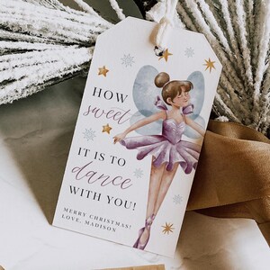 May include: A white gift tag with a watercolor illustration of a fairy dancing. The tag has gold stars and snowflakes and the text "How sweet it is to dance with you! Merry Christmas! Love, Madison".