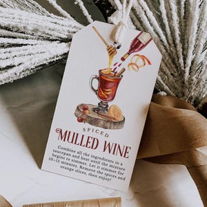 Könnte beinhalten: Ein Geschenkanhänger mit einer Aquarellillustration von Glühweinzutaten. Der Anhänger zeigt ein Glas Glühwein, eine Weinflasche, Honig und Zimtstangen. Der Text auf dem Anhänger lautet "Gewürzter Glühwein" mit Anweisungen.