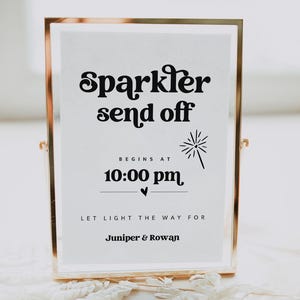 Könnte beinhalten: Ein goldfarbener Rahmen mit einem weißen Hintergrund und schwarzem Text, der "Sparkler send off Begins at 10:00 pm Let light the way for Juniper & Rowan" lautet. Das Schild zeigt eine kleine schwarze Feuerwerksgrafik.