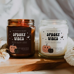Puede incluir: Dos velas en tarros de vidrio con tapas, etiquetadas como "The Pumpkin Palace" y "Spooky Vibes". Las etiquetas presentan un diseño de calabaza. Una vela está en un tarro marrón, la otra en un tarro transparente.
