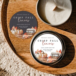 Puede incluir: Una vela redonda en lata con una etiqueta que dice "Whiskey Cedar Co. Crisp Fall Leaves" con una ilustración de acuarela de calabazas, hojas y libros. La vela es una vela de cera de coco con un aroma a especias de calabaza y roble. La vela pesa 300 gramos.