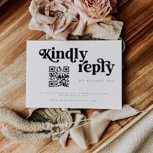 May include: A white card with black text that reads "Kindly reply by August 1st". A black and white QR code is above the text. The card is on a wooden tray with a pink flower and a piece of fabric.