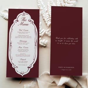 May include: Two rectangular menu cards in deep burgundy with white text. The left card features a decorative white frame containing the header The Menu and a list of courses. The right card displays a thank you message and the names Emily & Harrison.