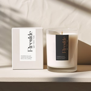 May include: A white candle with a black label that reads "Fireside Apple + Winter Teak" and "Pumpkin Palace Artisan Soy Wax Candle 60 hr | 10.5 oz | 300 g". The candle is in a clear glass jar and is sitting on a white surface.