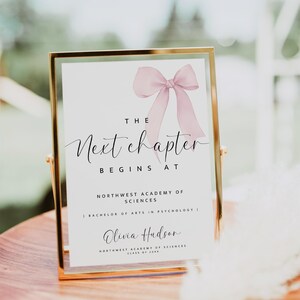 Puede incluir: Un cartel con marco dorado con un lazo de cinta rosa y el texto "THE Next chapter BEGINS AT NORTHWEST ACADEMY OF SCIENCES | BACHELOR OF ARTS IN PSYCHOLOGY | Olivia Hudson NORTHWEST ACADEMY OF SCIENCES CLASS OF 20XX"