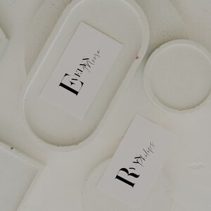 May include: Two white coasters with a white card on each. The card on the left has the text "Evelyn Moore" in black cursive writing. The card on the right has the text "Rita Phillips" in black cursive writing.