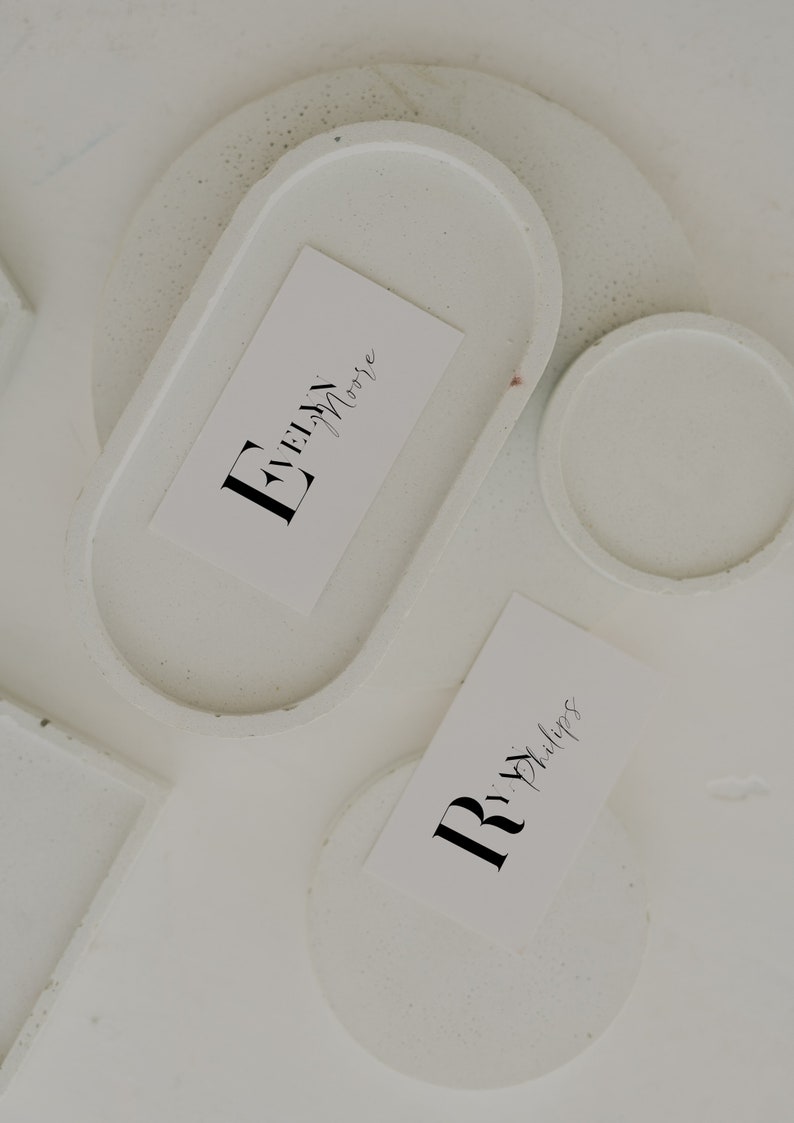 May include: Two white coasters with a white card on each. The card on the left has the text "Evelyn Moore" in black cursive writing. The card on the right has the text "Rita Phillips" in black cursive writing.