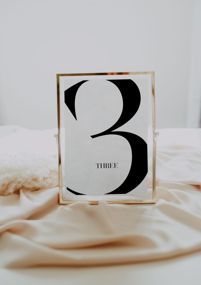 May include: A gold-framed table number with a black number three and the word "THREE" printed below it.