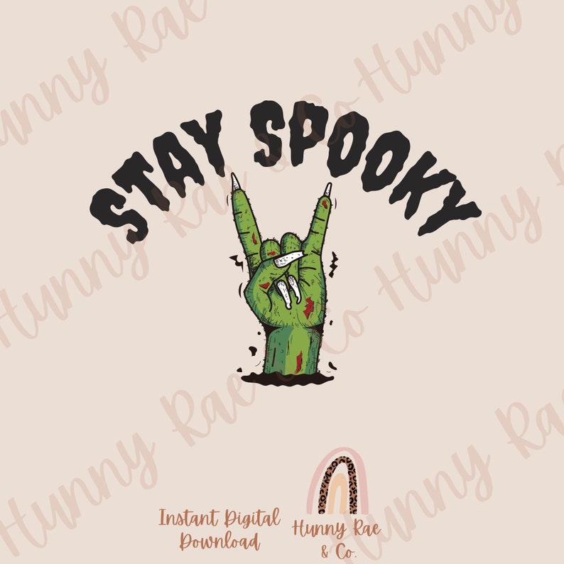 May include: A green zombie hand with long, sharp nails is making the rock and roll hand gesture. The hand is coming out of the ground. The text "STAY SPOOKY" is above the hand in black.