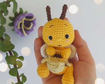 May include: A crocheted bee toy with yellow and brown fur, white wings, and black eyes. The bee is holding a small golden honeycomb.