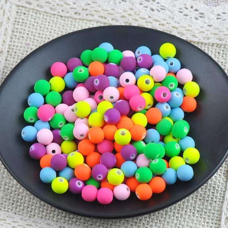 May include: A collection of colorful round beads in various bright colors, including pink, green, orange, yellow, blue, and purple. The beads are made of a smooth, matte material and have a small hole in the center.