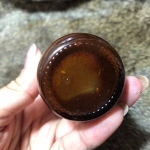 May include: Close-up of the bottom of a brown glass bottle with a clear liquid inside. The bottle has a textured rim.