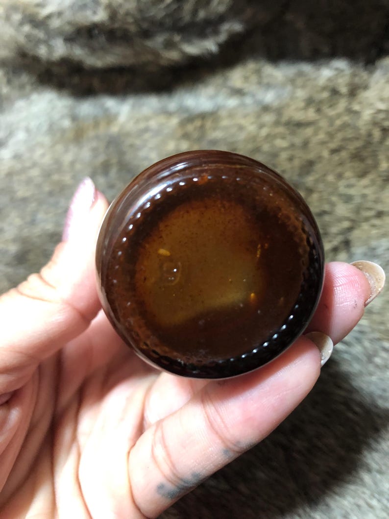 May include: Close-up of the bottom of a brown glass bottle with a clear liquid inside. The bottle has a textured rim.