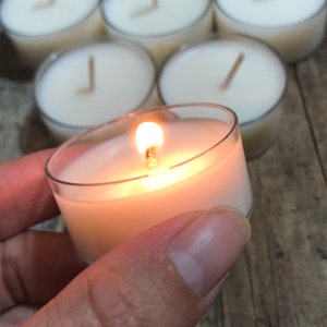 May include: A single tea light candle burning in a clear glass holder. The candle is surrounded by other unlit tea lights.