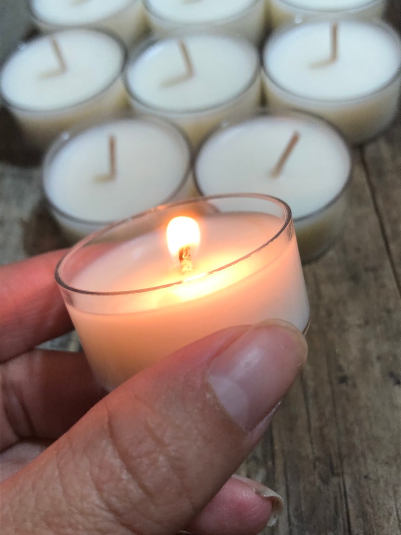 May include: A single tea light candle burning in a clear glass holder. The candle is surrounded by other unlit tea lights.