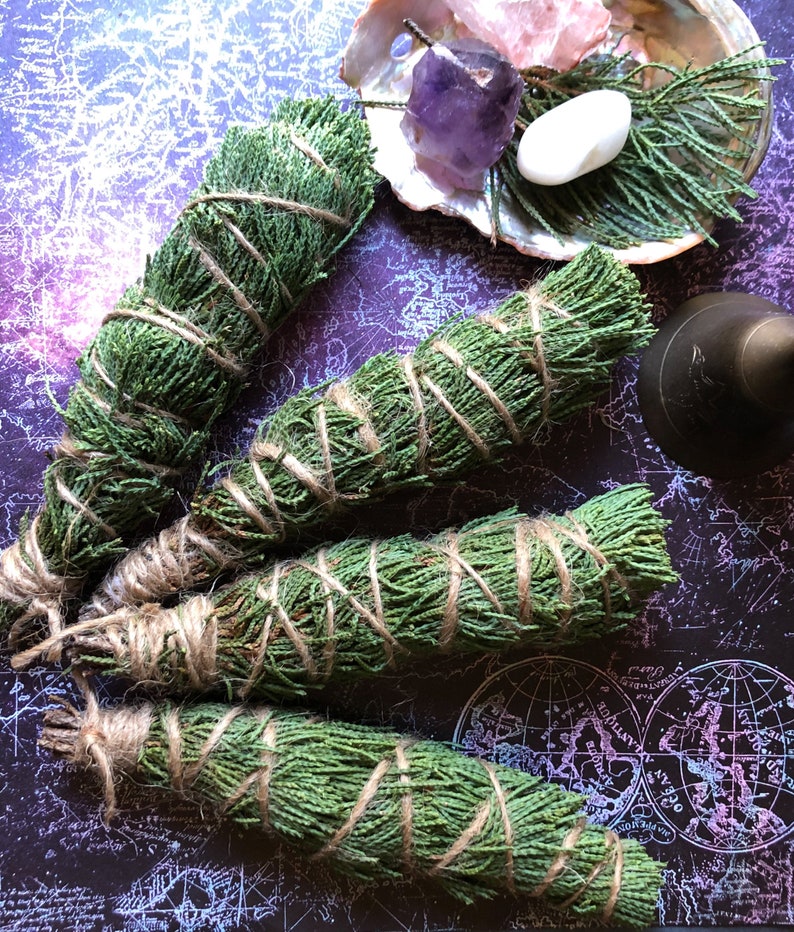 May include: Four bundles of dried cedar sage smudge sticks tied with twine. The bundles are arranged on a dark purple background with a map pattern.