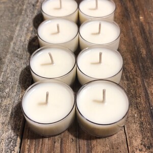 May include: Eight white unscented tea light candles in clear plastic containers on a wooden surface.