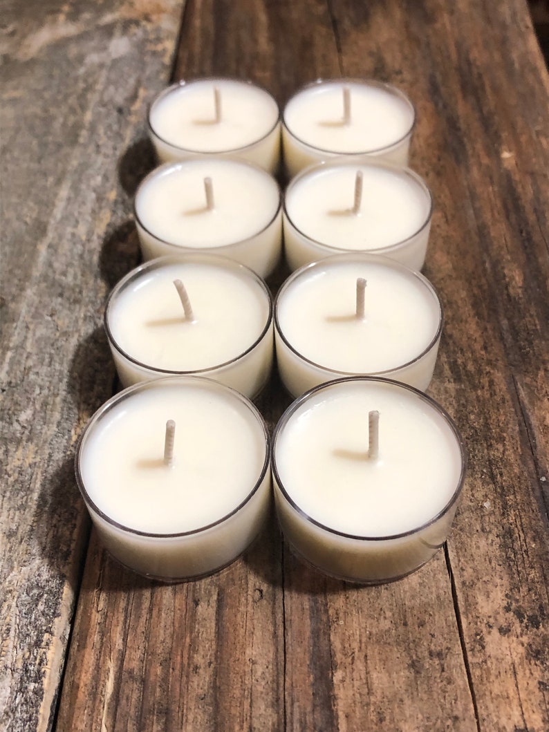 May include: Eight white unscented tea light candles in clear plastic containers on a wooden surface.