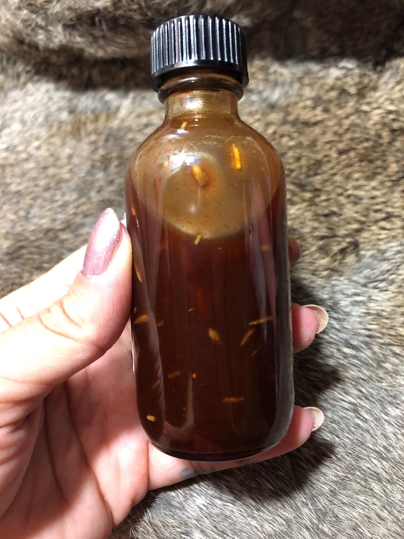May include: A small amber glass bottle with a black screw-on lid filled with a dark brown liquid and small, light brown particles.