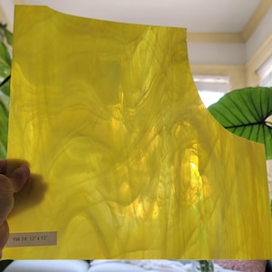 May include: A sheet of yellow stained glass, approximately 12 x 12 inches, with a wavy, textured pattern. The glass is held by a hand, and the label reads "YW 24 12" x 12".