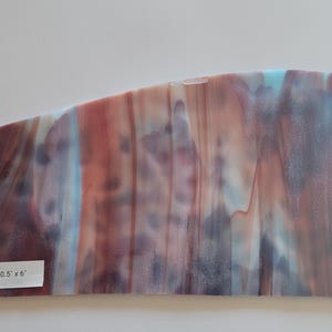 May include: A rectangular piece of stained glass with a blend of colors including red, blue, and purple. The glass measures 10.5 inches by 6 inches. The text "MX 90 10.5 x 6" is printed on a white label.