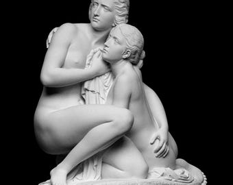 Puede incluir: Escultura de mármol blanco que representa a dos figuras en un tierno abrazo. Una figura está arrodillada, mientras que la otra está de pie, parcialmente cubierta. La escultura se encuentra sobre un fondo negro, resaltando los detalles de las figuras.