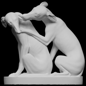 May include: A white ceramic sculpture of two dogs, one sitting and the other lying down, with their heads touching. The sculpture is on a white base.
