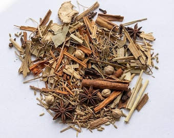 May include: A selection of dried herbs and spices, including star anise, cinnamon sticks, cardamom pods, and ginger. The mix features various shades of brown, tan, and green. The ingredients are scattered on a white surface, creating a visually appealing arrangement.