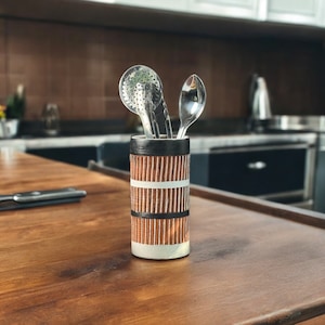 May include: A brown and white striped ceramic utensil holder with a silver spoon and a silver whisk inside.