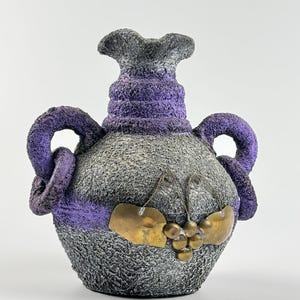 May include: A gray and purple ceramic vase with two handles and a grape design. The vase has a textured surface and gold accents.