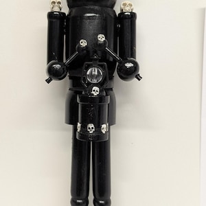 May include: Black wooden nutcracker figurine with skull and raven details. The figurine has a black top hat with a skull, two ravens, and small skulls on the shoulders. A lantern with skulls is in the center.