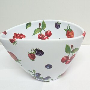 May include: White ceramic bowl with a fruit pattern. The bowl is decorated with illustrations of cherries, strawberries, raspberries, blueberries, and blackberries. The bowl has a wide, angled shape.