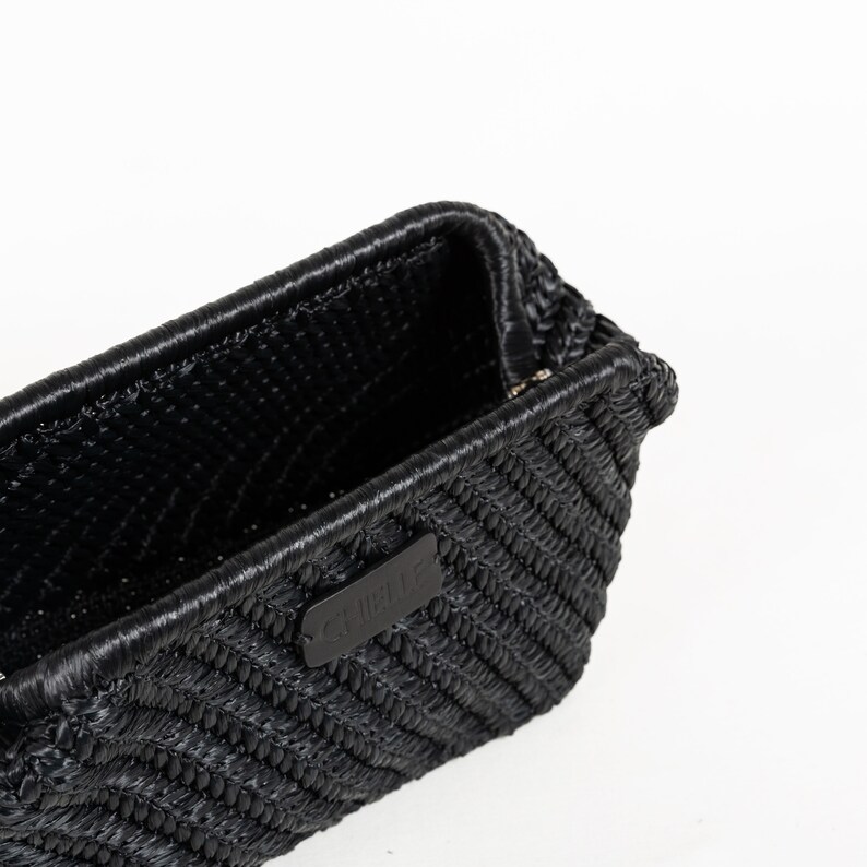 May include: A black woven handbag with a rectangular shape. The bag features a textured surface and a small, rectangular leather tag with white text. The bag is set against a white background.