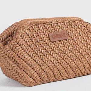 May include: A woven, light brown clutch bag with a rectangular shape and a rounded top. The bag features a textured, diagonal weave pattern and a small, brown leather tag with the word "CHELLE" embossed on it.