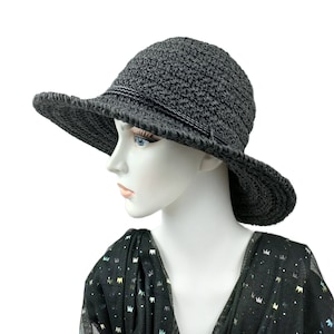 May include: A black crochet sun hat with a wide brim. The hat is worn by a mannequin with a black and white patterned scarf.