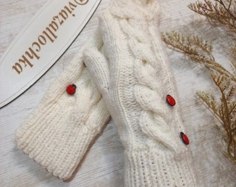 Puede incluir: Guantes sin dedos de punto blanco con un patrón de trenza y detalles de botones rojos.