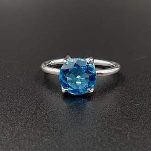 Può includere: Un anello d'argento con una grande pietra preziosa rotonda di topazio blu.